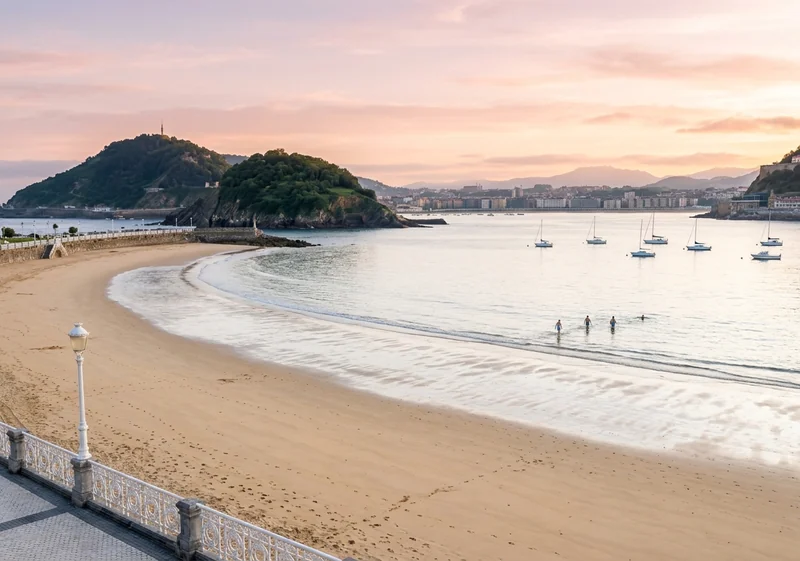 La Concha bay at dawn with swimmers, sailboats and Santa Clara island in San Sebastián