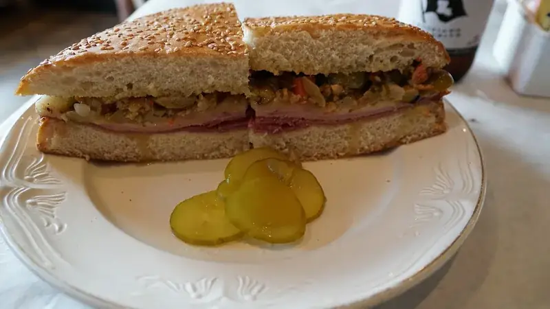 Half a muffuletta sandwich with olive salad and pickles on a plate in New Orleans