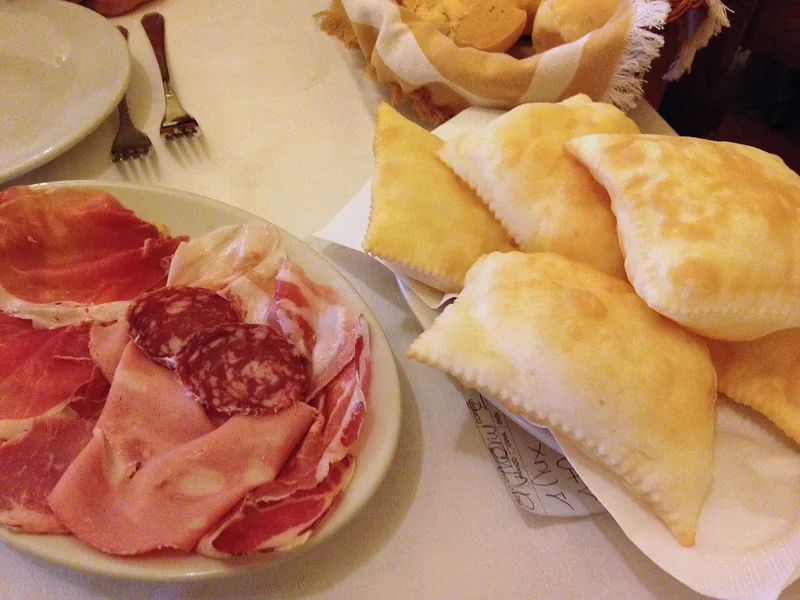 Sliced prosciutto, mortadella and salami beside a basket of puffed gnocco fritto in Emilia-Romagna