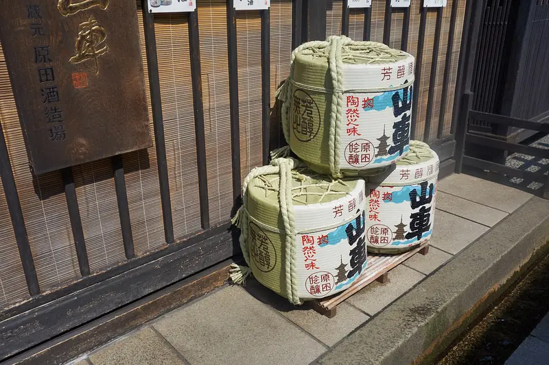 Straw-wrapped komodaru sake barrels stacked outside a wooden sake brewery in Takayama, Japan